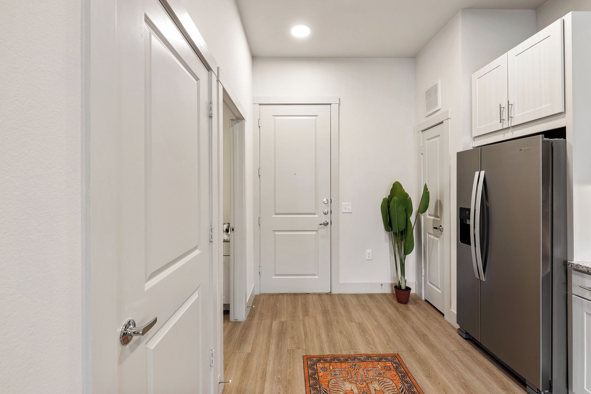 A modern kitchen with white cabinetry, a stainless steel refrigerator, and a wooden floor.