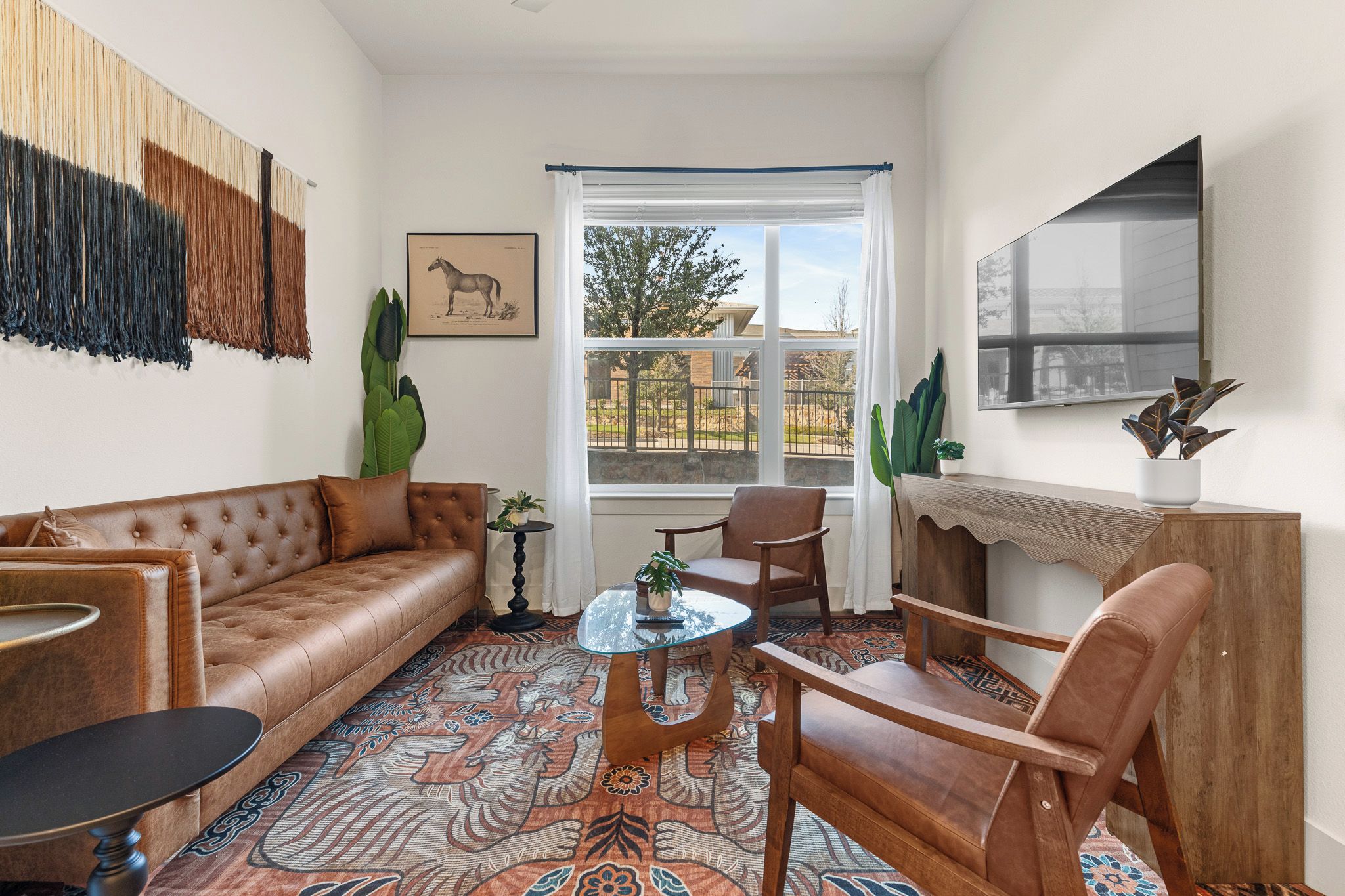 A living room with a brown leather sofa, a wooden coffee table, a patterned rug, and a large window with a view of the outdoors.