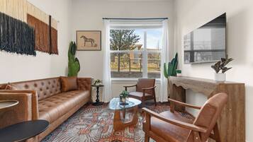 A living room with a brown leather sofa, a wooden coffee table, a patterned rug, and a large window with a view of the outdoors.