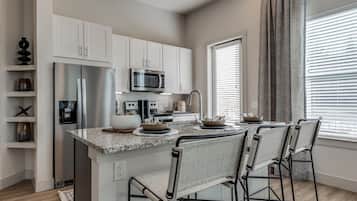 A modern kitchen with white cabinets, stainless steel appliances, a granite countertop, and bar stools.