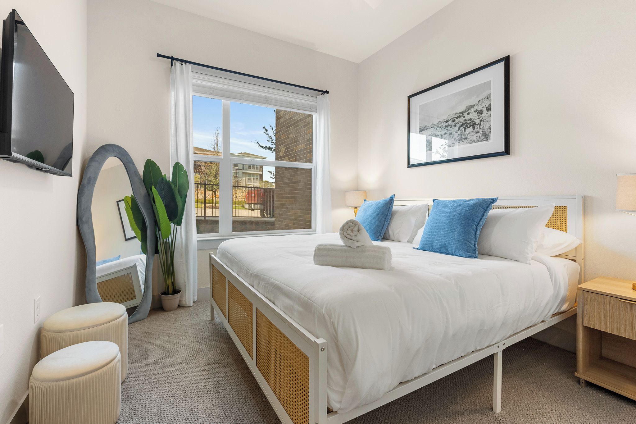 A bedroom with a bed, bedside table, lamp, window, and a framed picture on the wall.