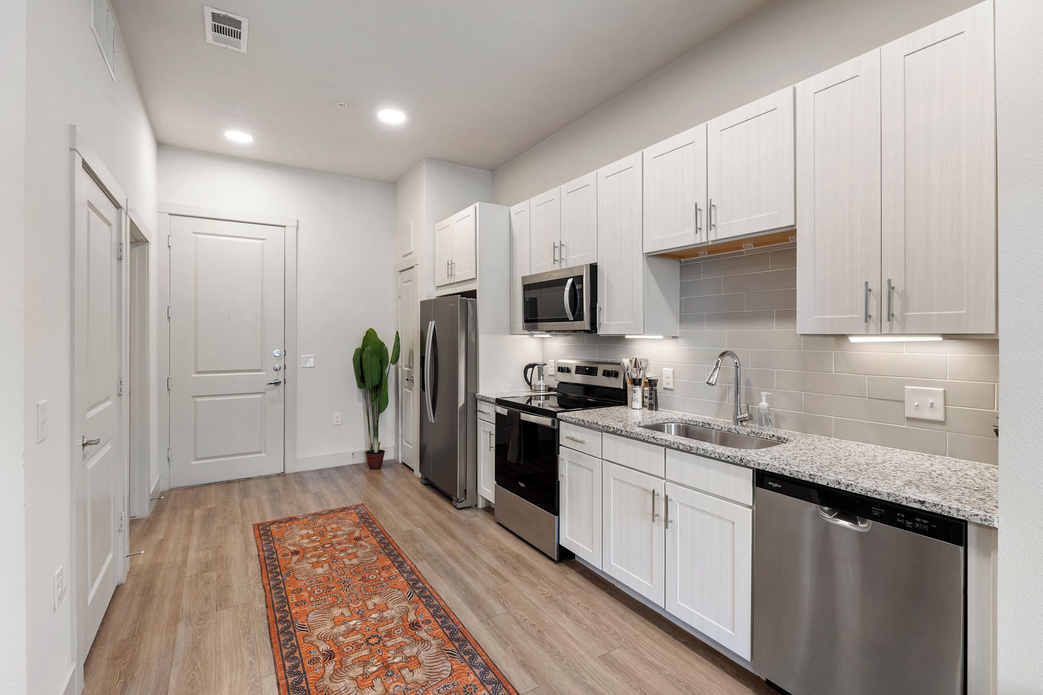 A modern kitchen with white cabinets, stainless steel appliances, and a granite countertop.