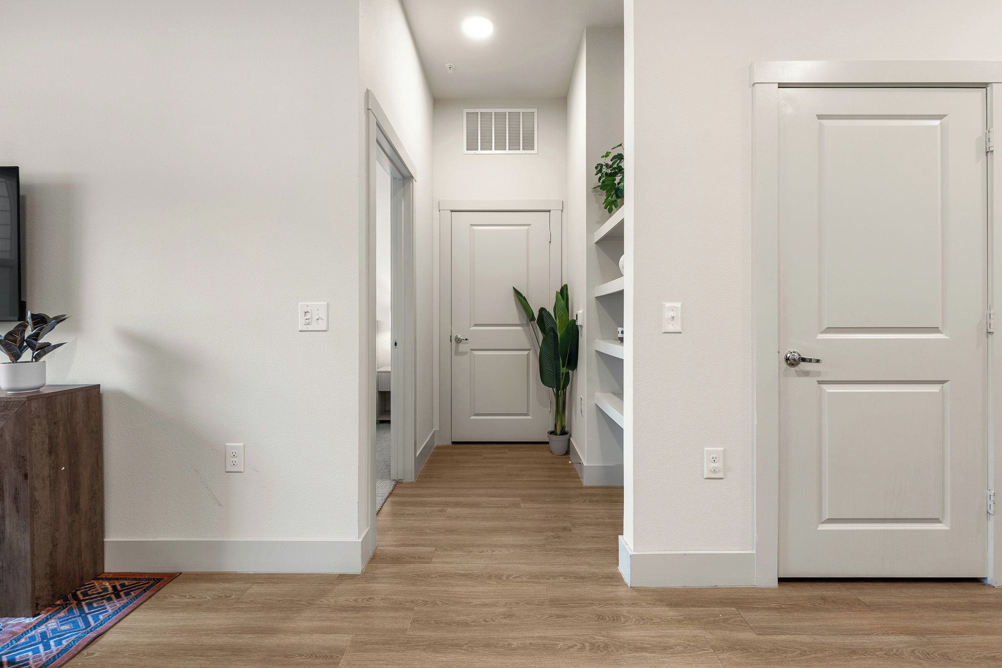 A hallway with wooden flooring, white walls, and doors leading to other rooms.