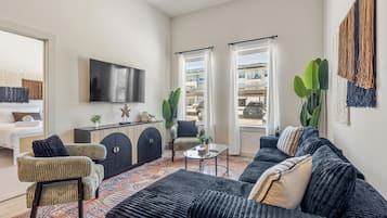 A modern living room with a large flat-screen TV, a sofa set, a coffee table, and a patterned rug.
