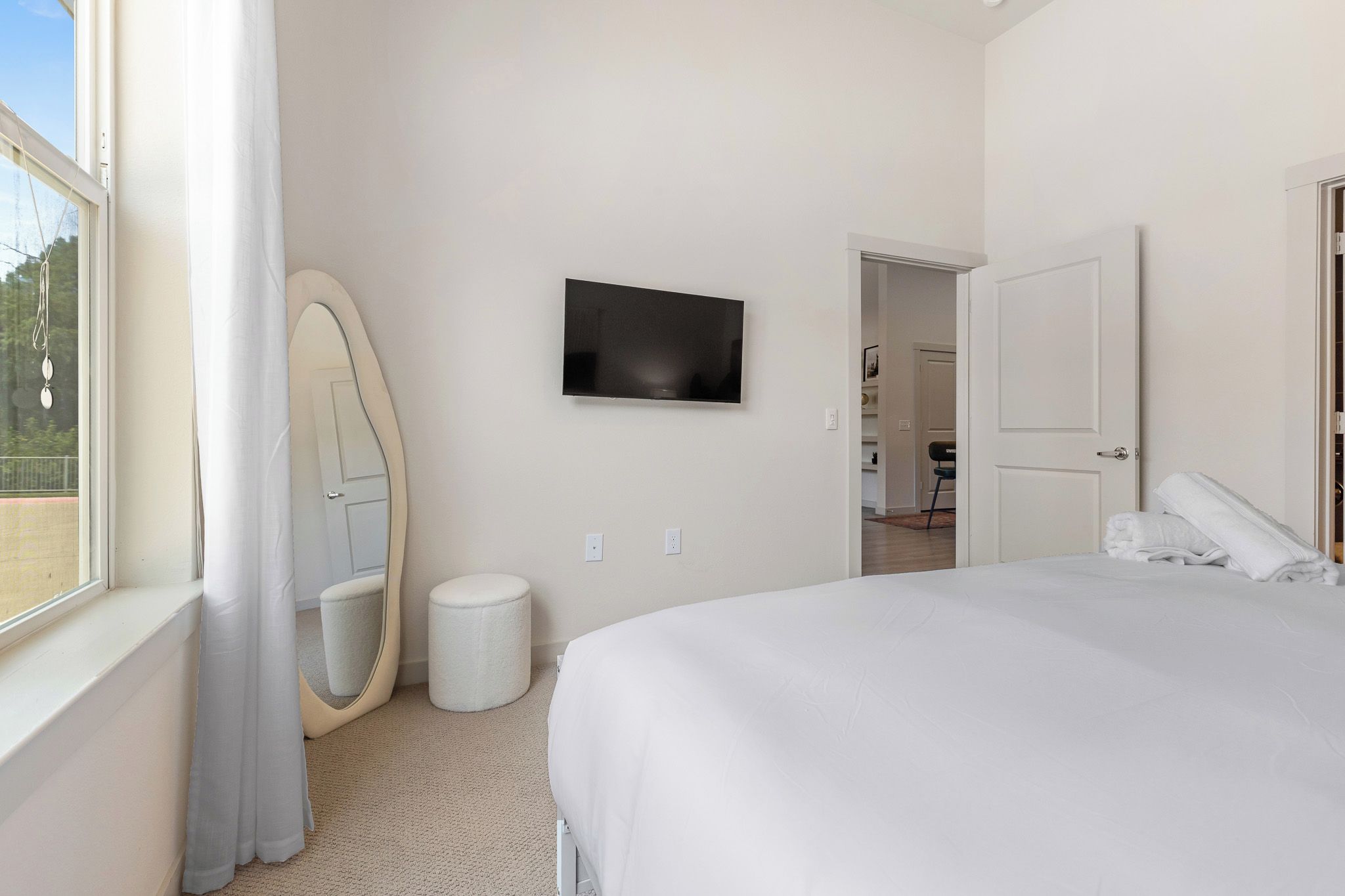 A hotel room with a bed, a television on the wall, a door, and a window.