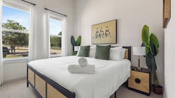 A bedroom with a bed, a nightstand, a lamp, a painting, and a window with curtains.