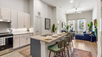 A modern kitchen with a central island, bar stools, and a dining area with a blue sofa.