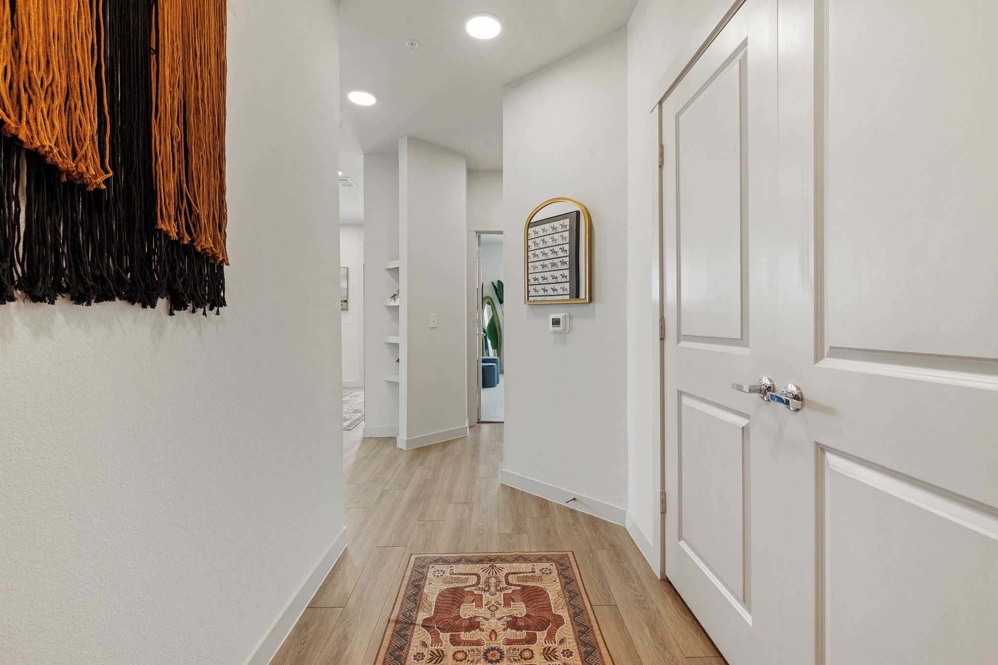 A hallway with white walls, a patterned rug, and a door with a mirror.