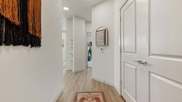 A hallway with white walls, a patterned rug, and a door with a mirror.