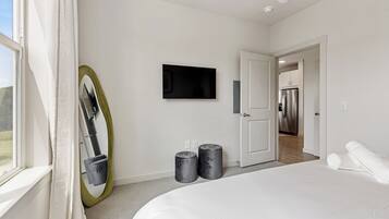 A modern bedroom with a large bed, a television mounted on the wall, and a door leading to a kitchen.