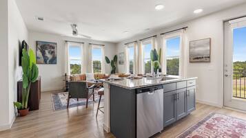 A modern kitchen with a central island, a dining area with a sofa and chairs, and large windows with curtains.