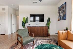 A living room with a sofa, a chair, a TV mounted on the wall, and a decorative horse sculpture. - McKinney 2BR | Kitchen & Stylish Layout CSA 5201 (McKinney)