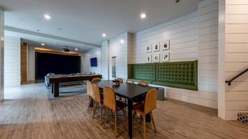 A modern dining area with a pool table, a green cushioned bench, and a dining table with chairs.