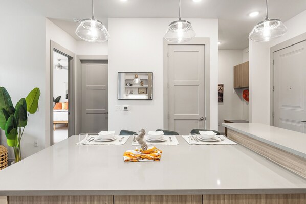 Una cocina moderna con una isla central, luces colgantes y un área de comedor con sillas y una mesa para dos.