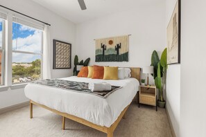 Een slaapkamer met een groot bed, een nachtkastje, een wandtapijt en een raam met uitzicht.