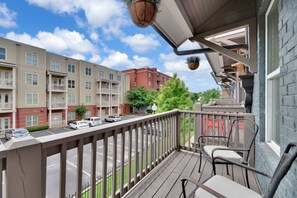 A balcony with a view of a multi-story building, a street with parked cars, and a clear sky. - 3bed/3bth Just Minutes from Downtown (Nashville)