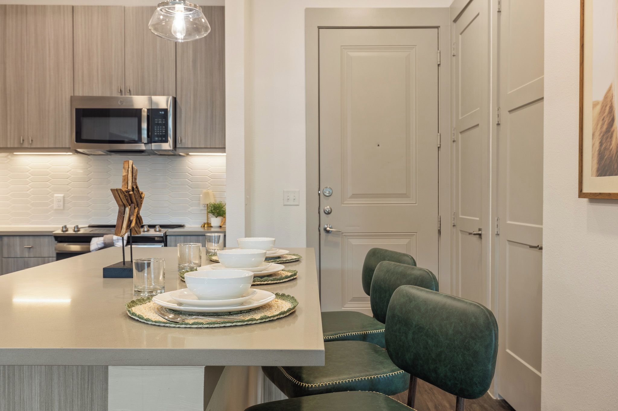 A modern kitchen with a central island, stainless steel appliances, and a dining area with green upholstered chairs.