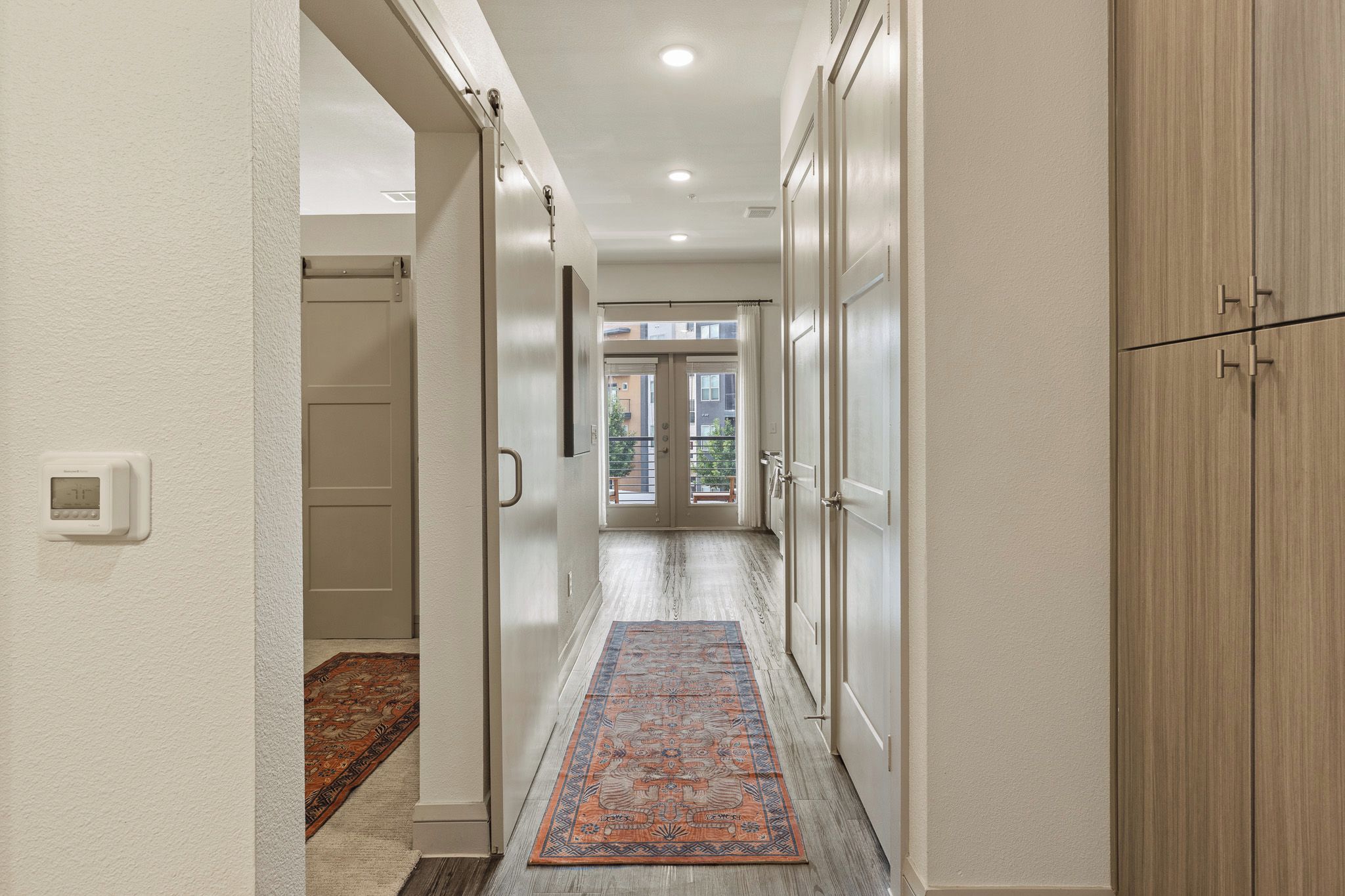 A hallway with a patterned rug, a thermostat, and a view of the outside.