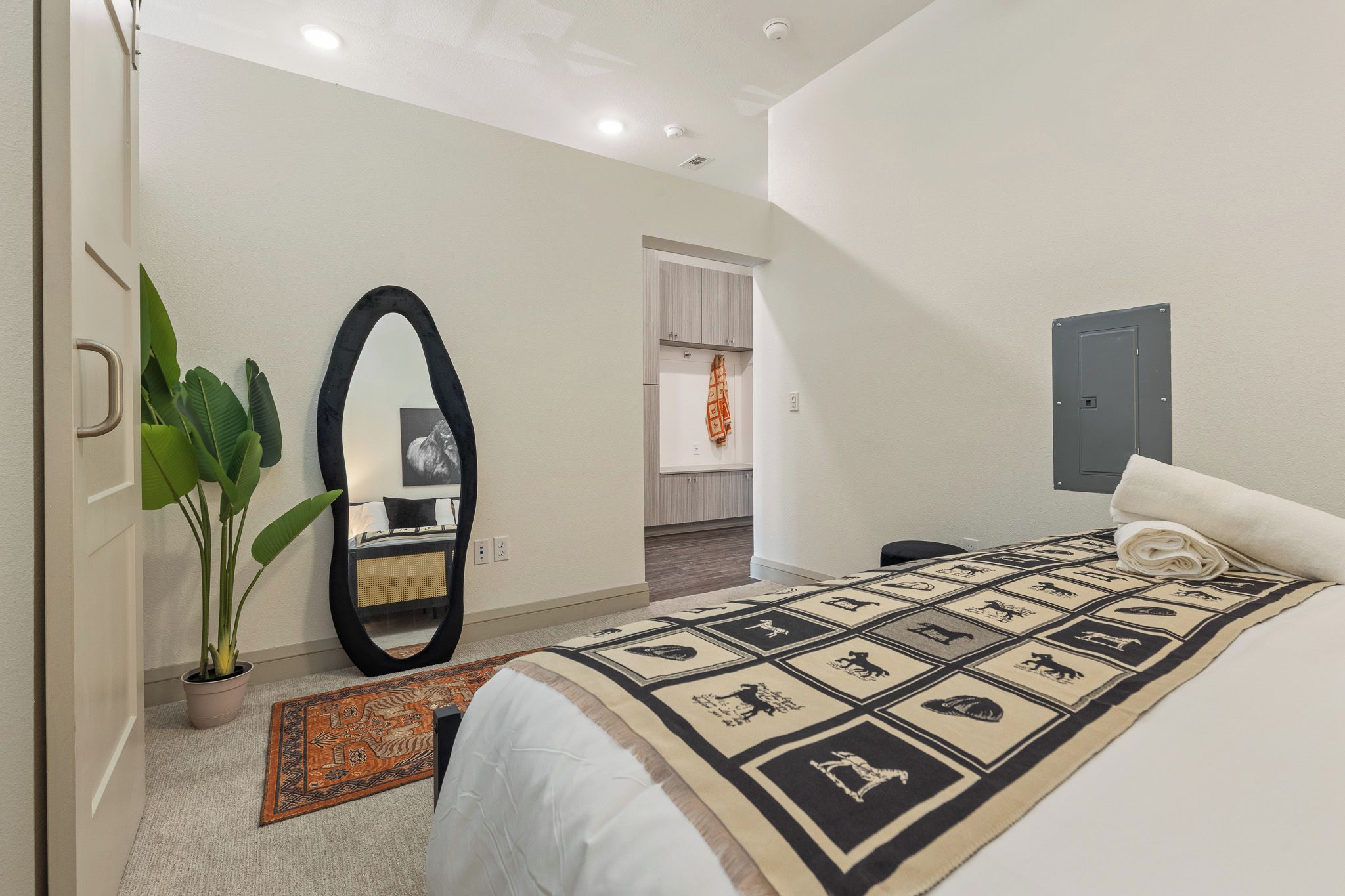 A modern bedroom with a large bed, a mirror, a potted plant, and a patterned rug.