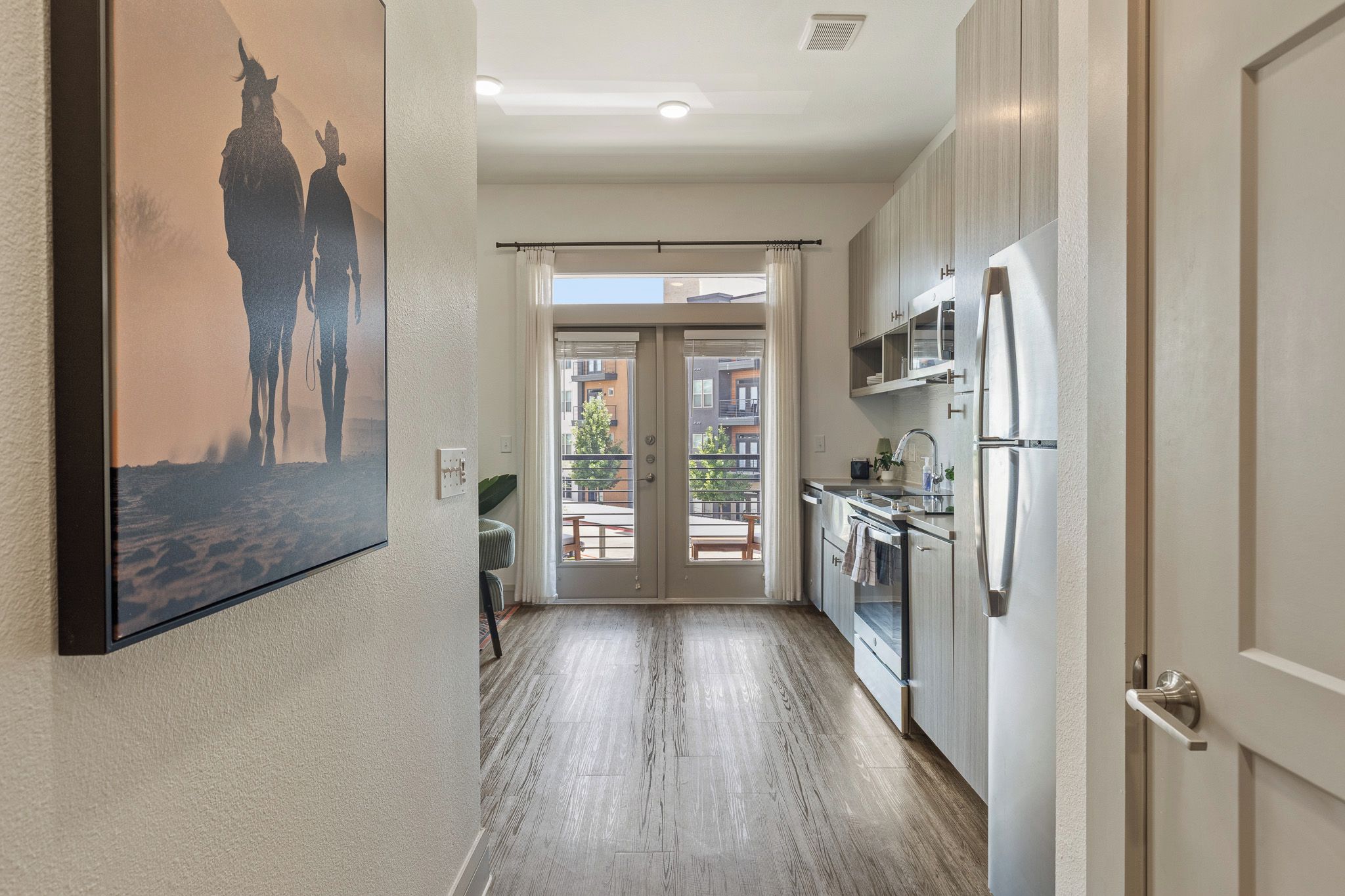 Una cocina moderna con un refrigerador de acero inoxidable, una zona de comedor con mesa y sillas, y un ventanal con vistas a la calle.