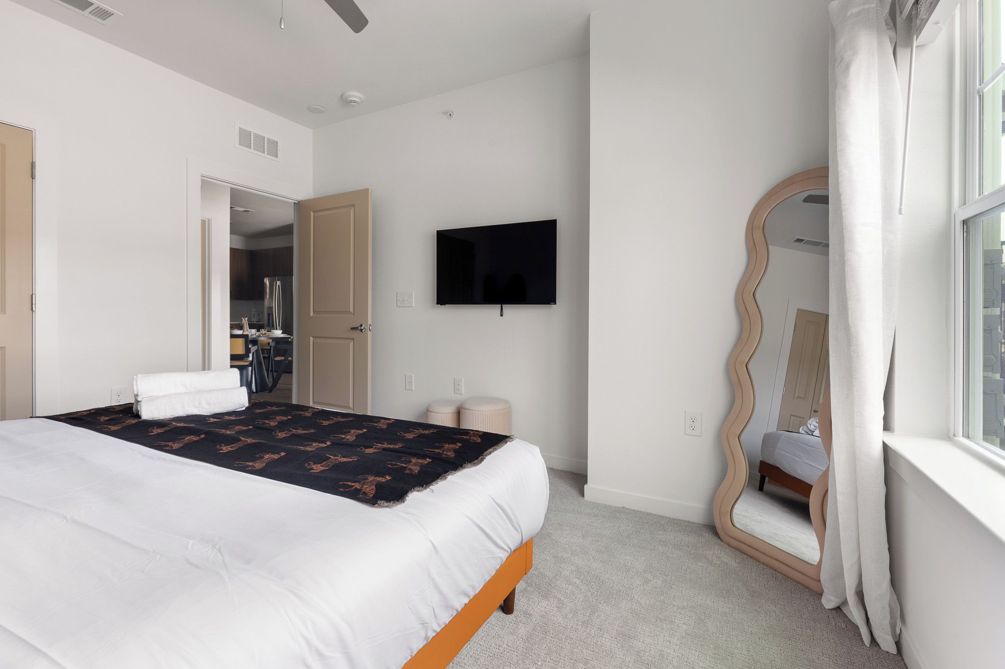 A hotel room with a bed, a television, a mirror, and a window.