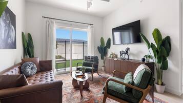 A living room with a sofa, armchair, coffee table, and a TV mounted on the wall.