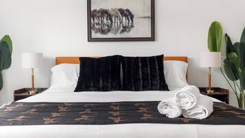 A hotel room with a bed, two nightstands, a painting, and potted plants.