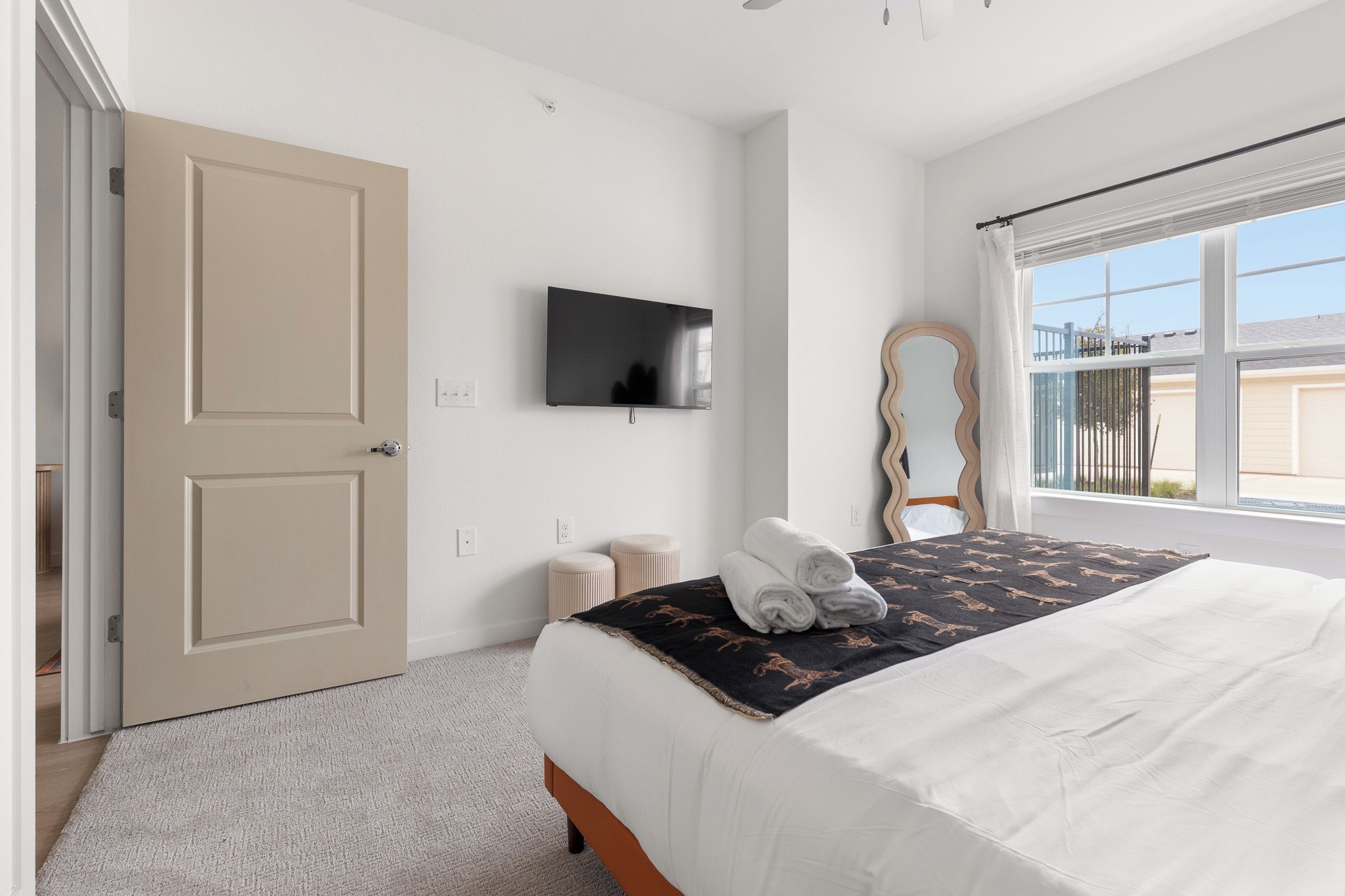 Un dormitorio con una cama, televisor, espejo y ventana.