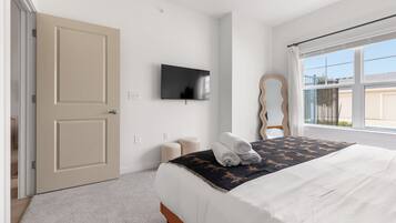 Un dormitorio con una cama, televisor, espejo y ventana.