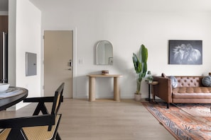 Een moderne woonkamer met een bruine leren bank, een ronde houten tafel, een klein bijzettafeltje, een spiegel en een kamerplant.