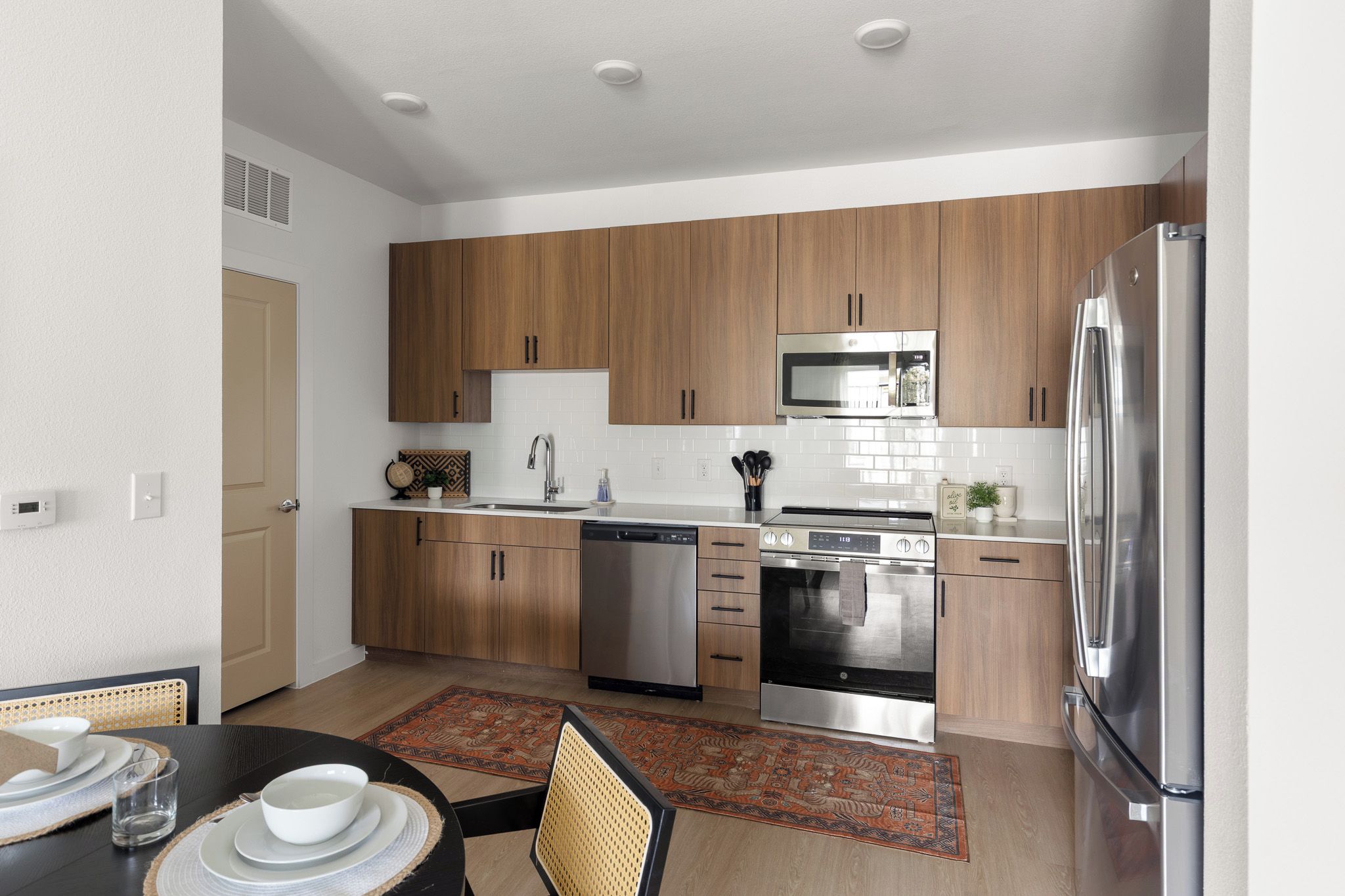 A modern kitchen with wooden cabinets, stainless steel appliances, and a dining area with a table set for two.