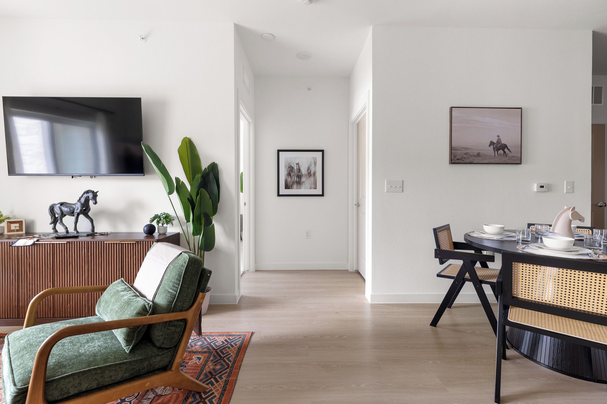 A modern living room with a television, a horse sculpture, and a dining area with a table and chairs.