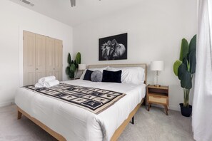 Une chambre à coucher bien rangée, avec un lit, des tables de chevet, une œuvre d’art accrochée au mur et une plante en pot.