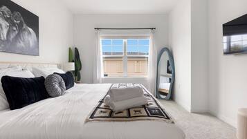 A bedroom with a large bed, a window with a view of a building, a mirror, and a painting on the wall.