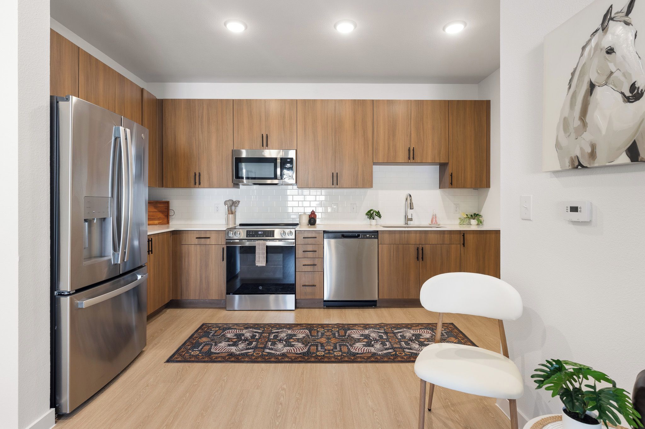 A modern kitchen with stainless steel appliances, wooden cabinets, and a white chair.