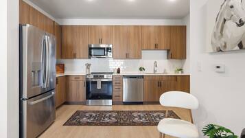 A modern kitchen with stainless steel appliances, wooden cabinets, and a white chair.