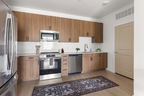 Une cuisine moderne avec des meubles en bois, des appareils électroménagers en acier inoxydable et un tapis à motifs.