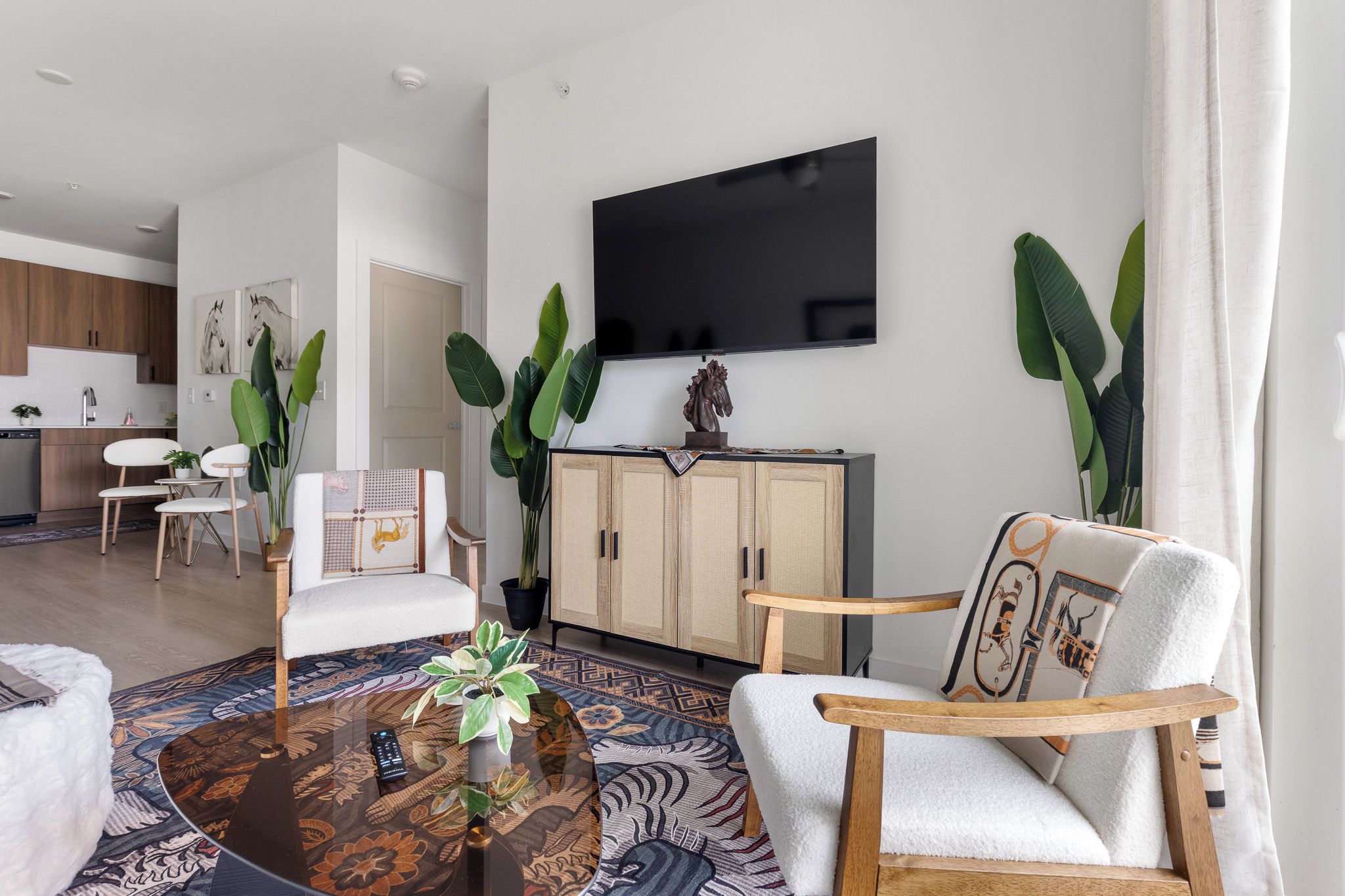 Una sala de estar moderna con televisor de pantalla plana, asientos cómodos, una mesa de centro y una cocina al fondo.