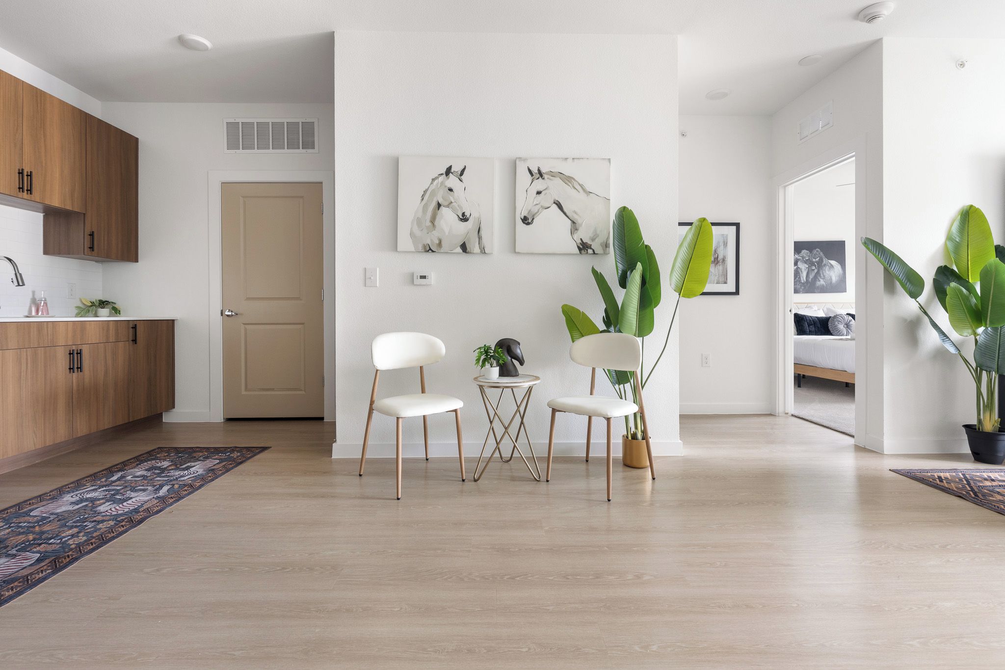 A modern living room with a wooden floor, white walls, and a dining area with two white chairs and a small table.