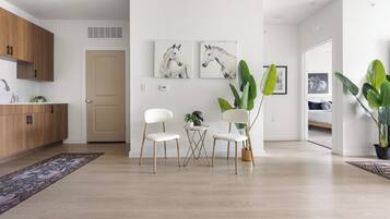 A modern living room with a wooden floor, white walls, and a dining area with two white chairs and a small table.