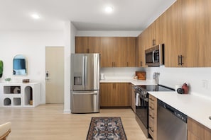 Una cocina moderna con electrodomésticos de acero inoxidable, armarios de madera y encimera blanca.