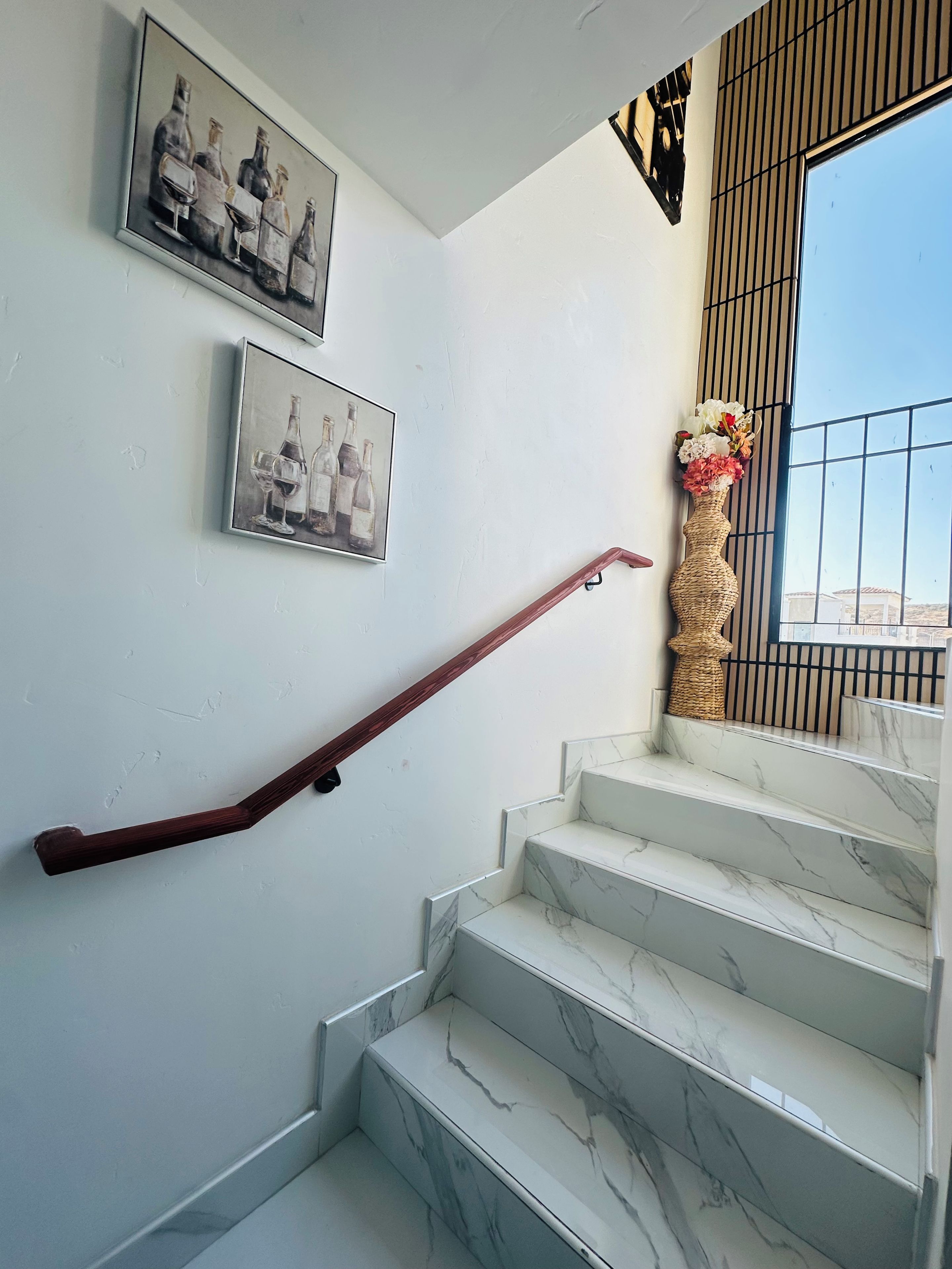 A staircase with marble steps and a wooden handrail, flanked by two framed pictures on the wall.