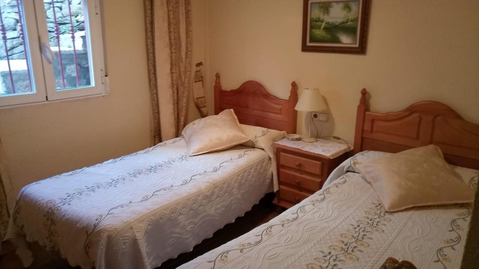 Un dormitorio con dos camas individuales, una mesita de noche con lámpara y una ventana con cortinas.