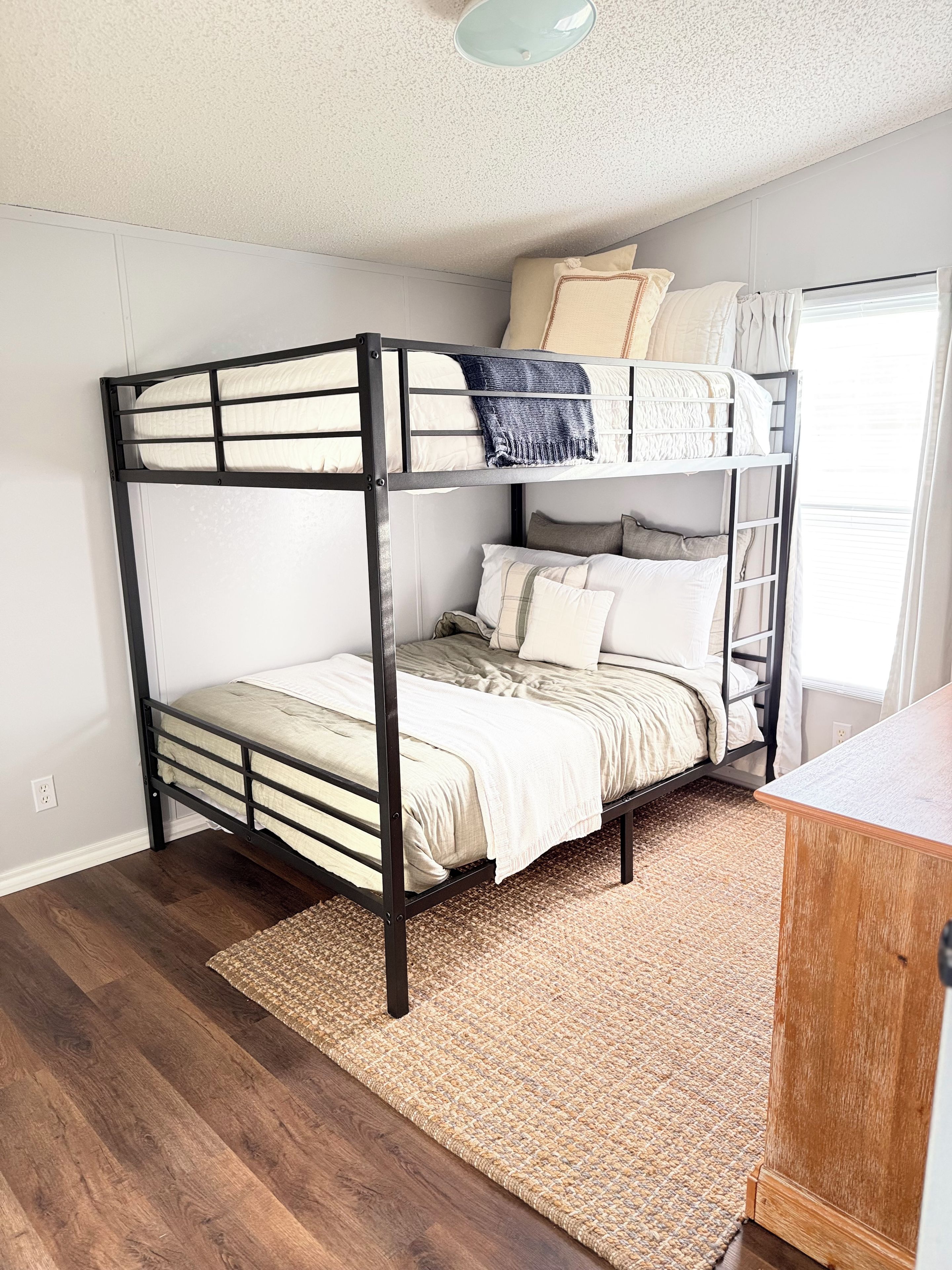 A bunk bed with a wooden frame, a woven rug, and a wooden desk.
