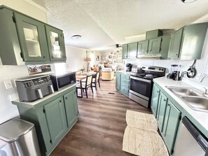 A kitchen with green cabinets, a microwave, a stove, and a dishwasher. - The Cozy Olive Retreat – Peaceful Country Living – 3 Bedroom, 2 Bath (Santa Fe)