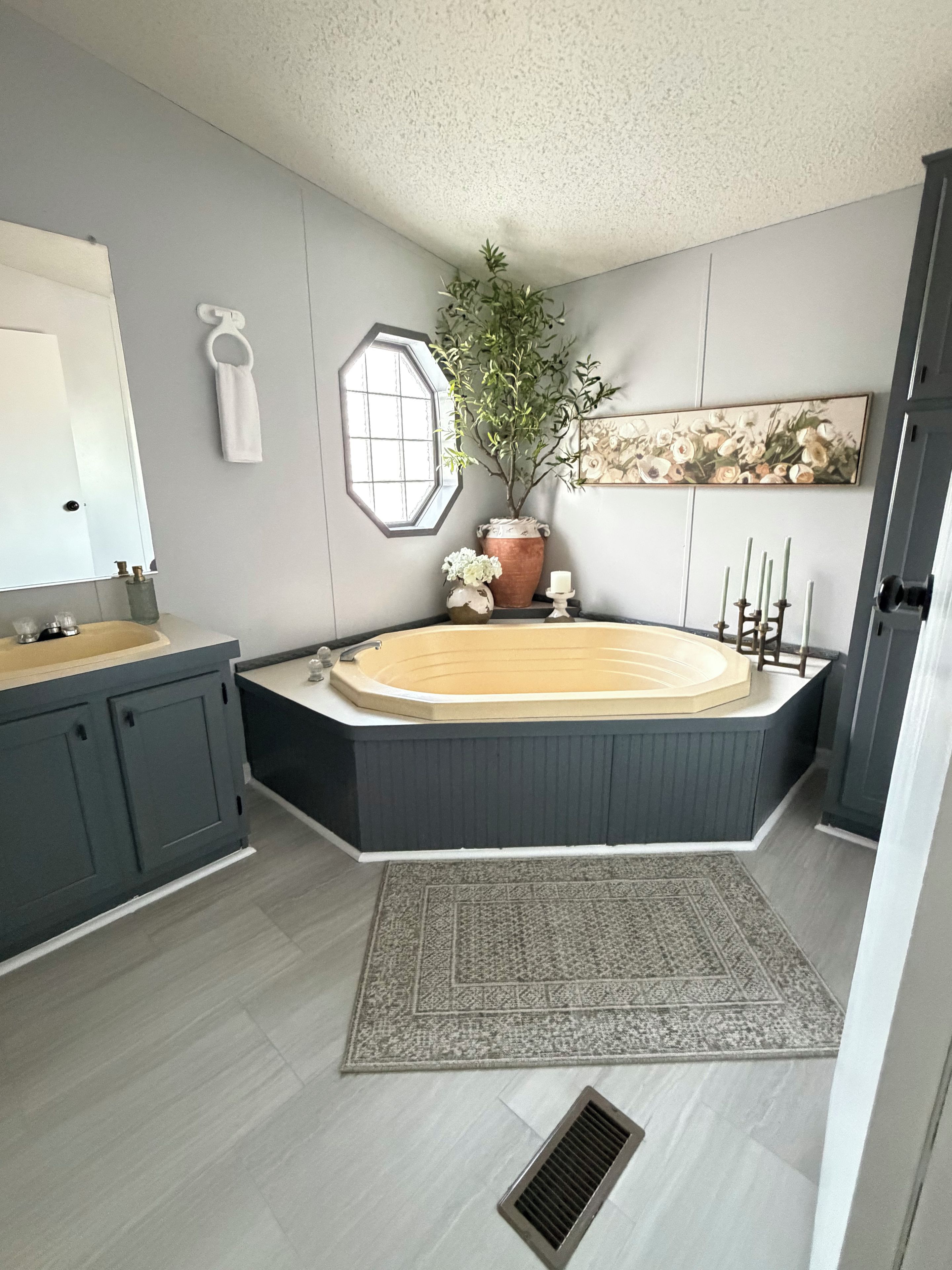 A modern bathroom with a freestanding bathtub, a large mirror, a potted plant, and a decorative wall piece.