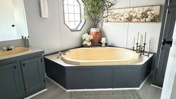 A modern bathroom with a freestanding bathtub, a large mirror, a potted plant, and a decorative wall piece.