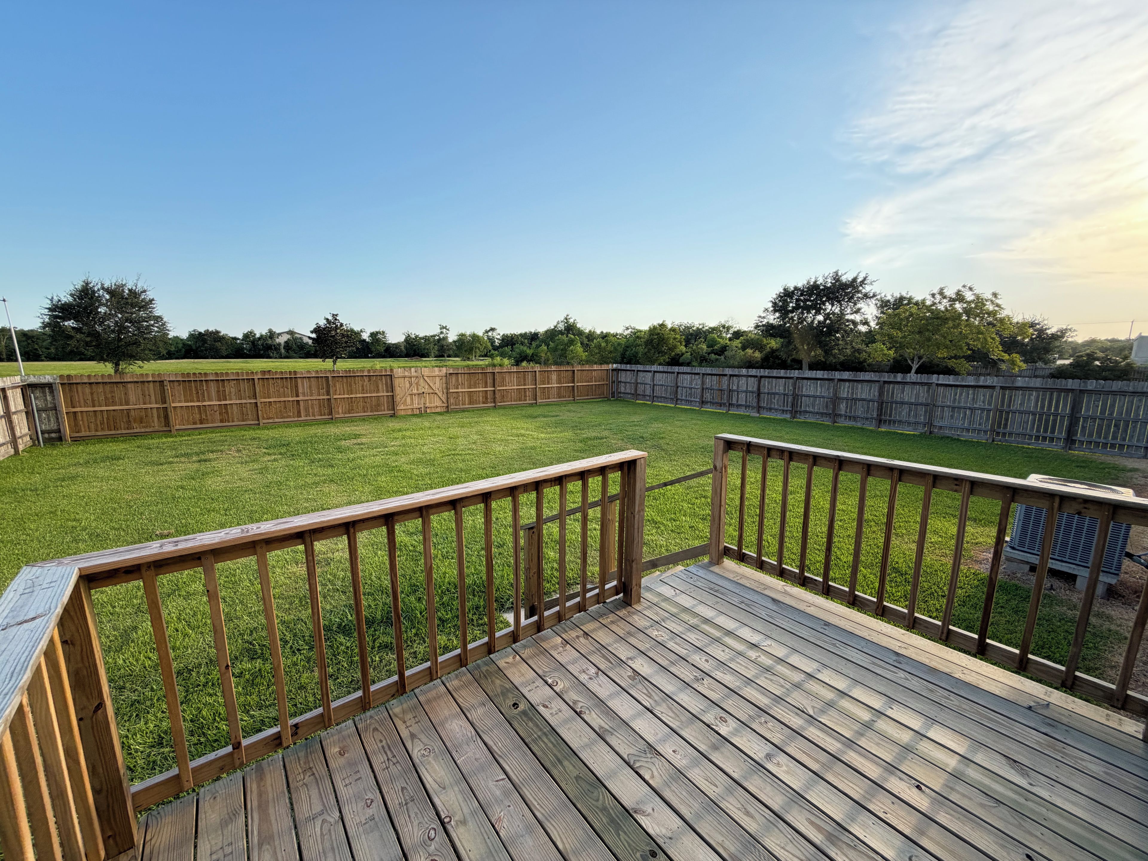 Une terrasse en bois offrant une vue sur un jardin verdoyant, délimité par une clôture en bois.