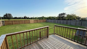 Une terrasse en bois offrant une vue sur un jardin verdoyant, délimité par une clôture en bois.