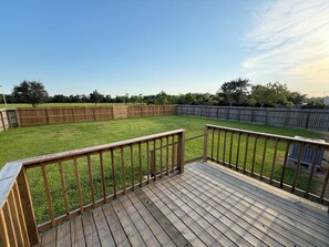 A wooden deck with a view of a grassy backyard enclosed by a wooden fence.
